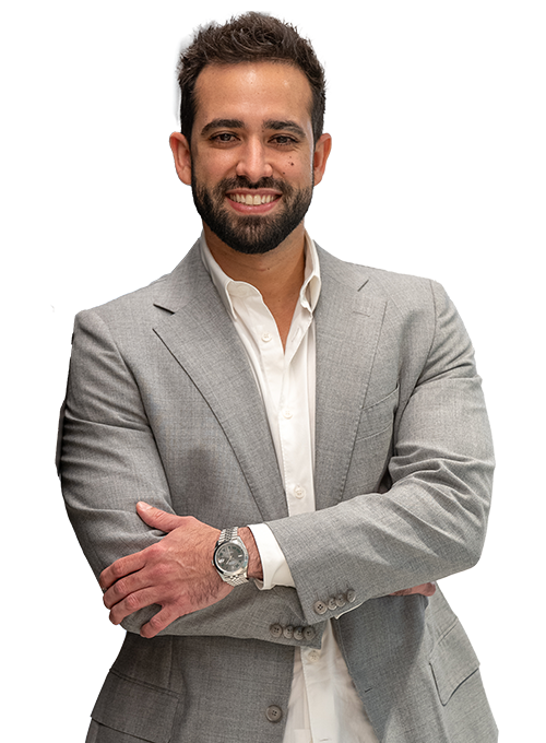 A man with a beard, wearing a gray suit and white shirt, smiles while crossing his arms. He is wearing a watch on his left wrist. The background is white.