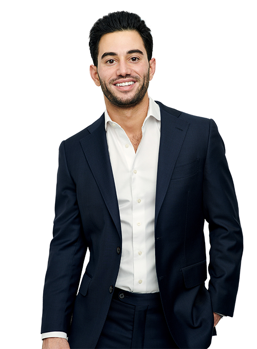 A smiling man with short dark hair wearing a white shirt and a dark suit, standing against a plain background.