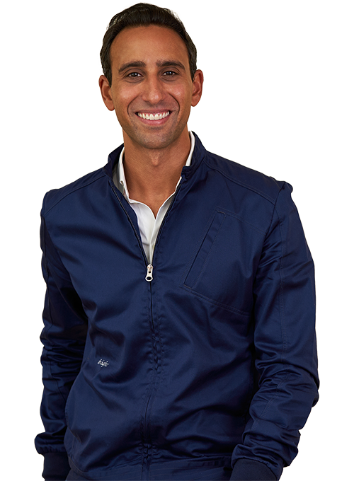 A man in a navy jacket and white shirt smiles at the camera. He stands against a plain background.