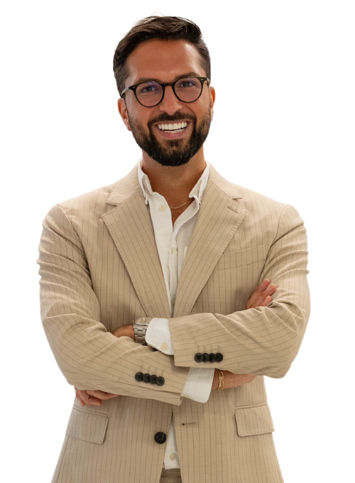 A man with a beard and glasses, wearing a beige pinstripe suit and a white shirt, is smiling with his arms crossed in front of him.