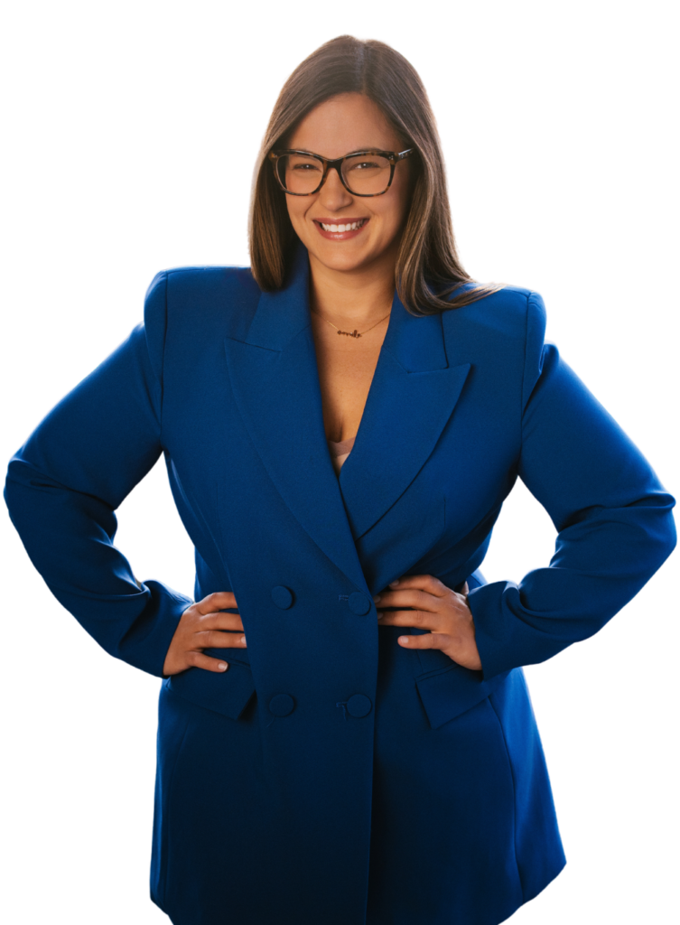 A woman wearing a blue blazer and glasses smiles confidently with her hands on her hips.