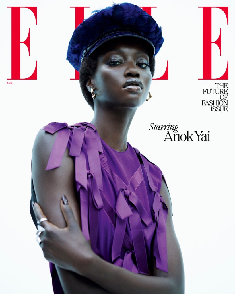 A model poses on the cover of Elle magazines The Future of Fashion issue. She wears a purple top with ribbon details and a navy cap. Text reads Starring Anok Yai. The background is white.