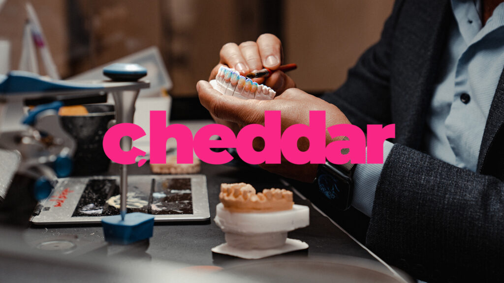 Person working on dental molds at a table with various tools and materials, the word cheddar in bold pink text overlays the image.