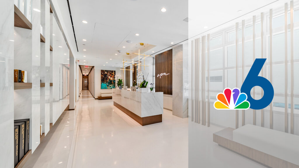 Modern office lobby with a marble reception desk, decorative shelving with books, and contemporary art on the walls. A large 6 logo with colorful peacock feathers is overlaid on the right side of the image.