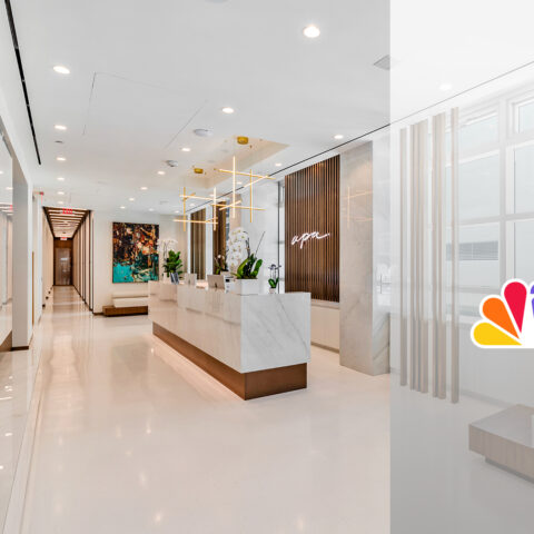 Modern office lobby with a marble reception desk, decorative shelving with books, and contemporary art on the walls. A large 6 logo with colorful peacock feathers is overlaid on the right side of the image.